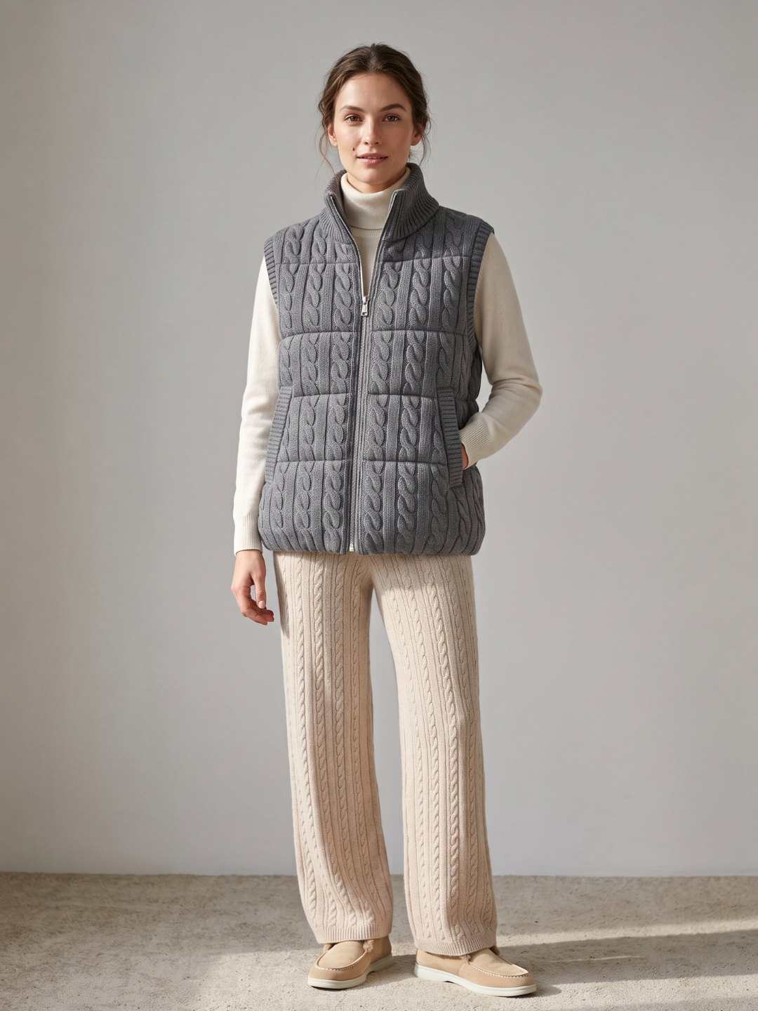 Model wearing the grey cashmere cable knit down vest over an ivory roll-neck with beige cable knit trousers – Dolcie London